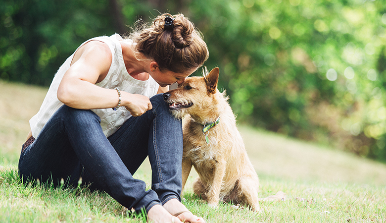 Frau kuschelt mit ihrem Hund im Gras sitzend