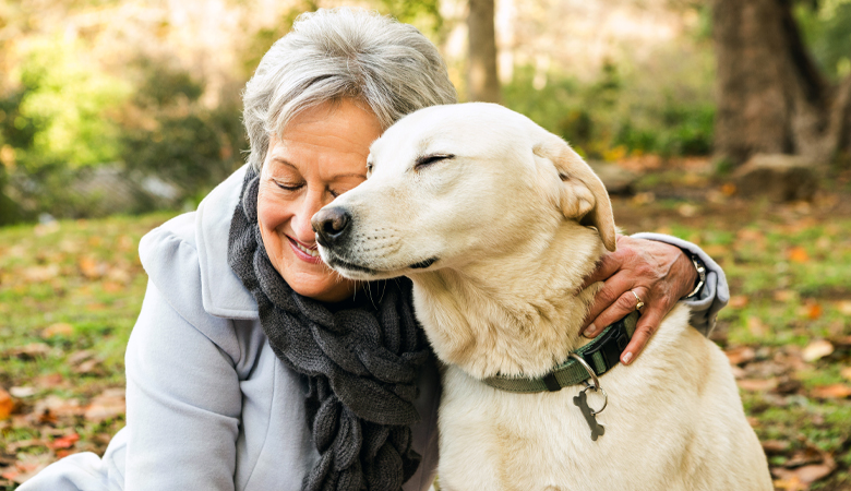 Oudere vrouw zit met oudere hond buiten in het bos