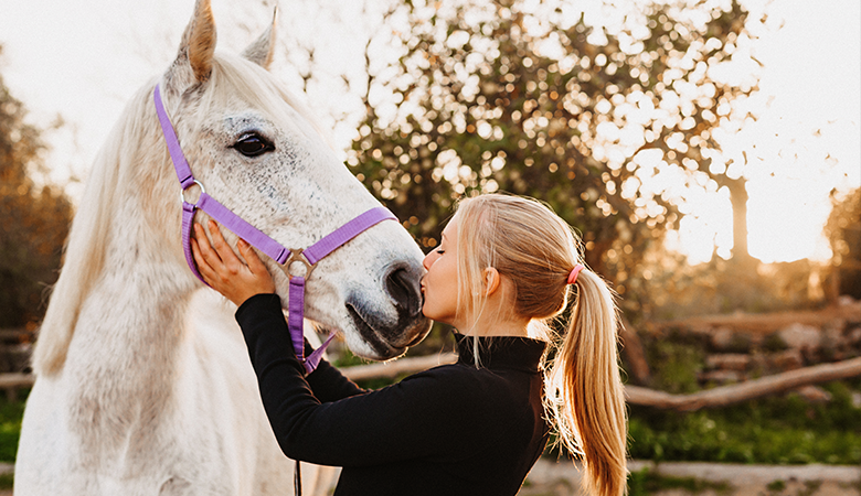 vrouw geeft kus op de neus van wit paard