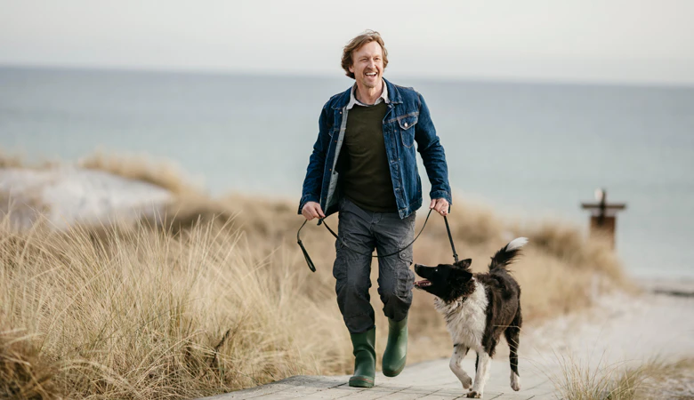Mann geht mit Hund am Strand spazieren.