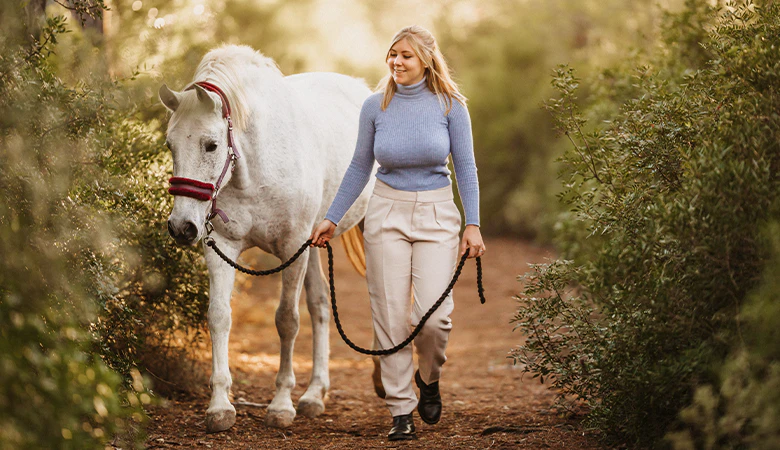 Vrouw loopt naast wit paard 